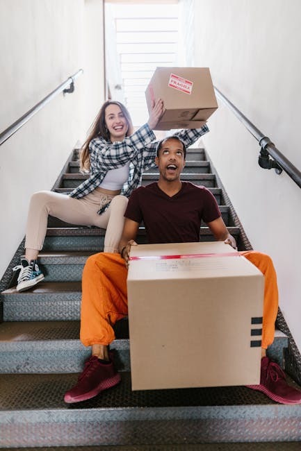 Inside a room used for home relocation, three cardboard moving boxes of varying sizes are stacked near a wooden cabinet. The boxes are sealed with clear packing tape and appear ready for transport. A 